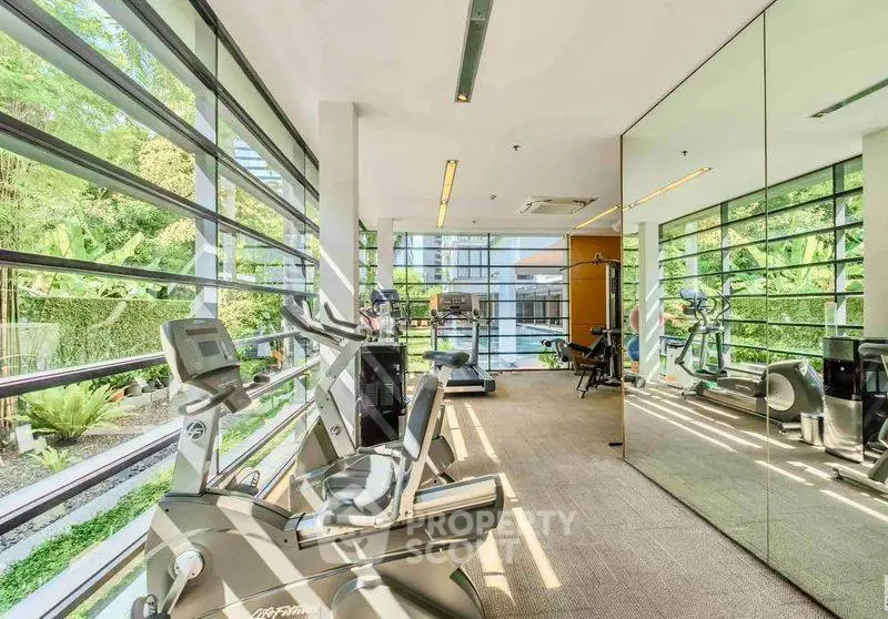 Modern gym with large windows and lush garden view, featuring state-of-the-art exercise equipment.