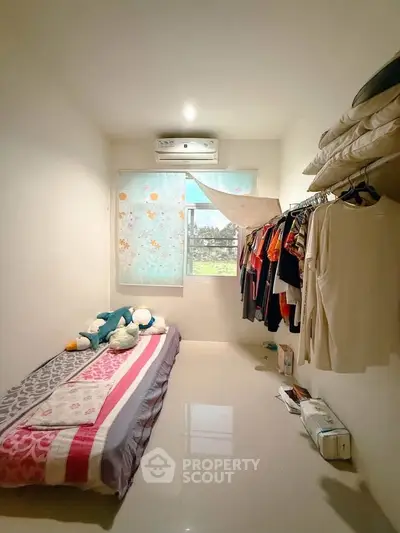 Cozy bedroom with minimalist decor and natural light, featuring a single bed and organized clothing storage.