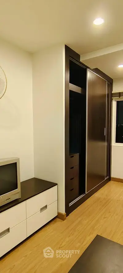 Modern bedroom with sleek wardrobe and TV unit, featuring warm wooden flooring and ambient lighting.