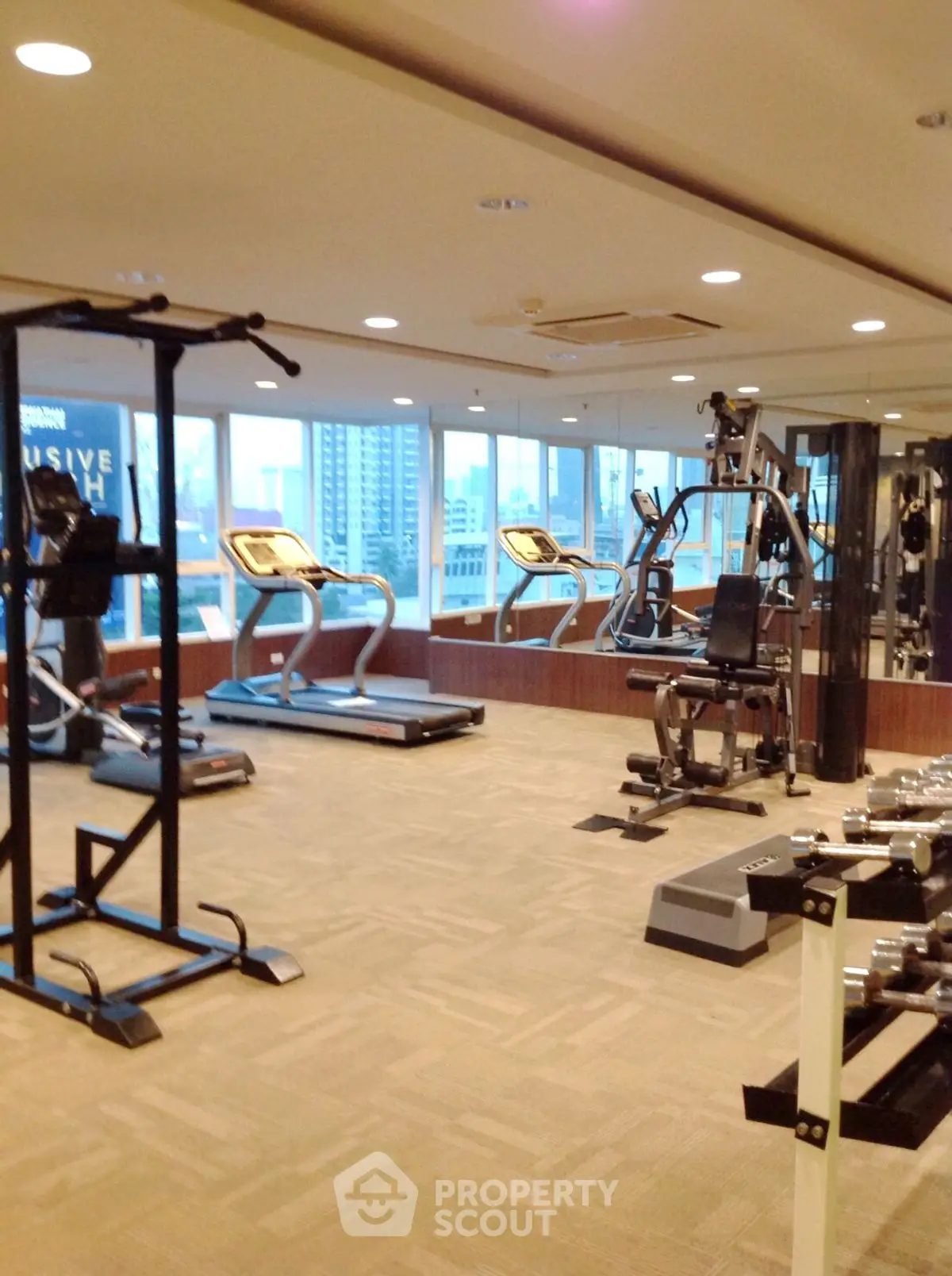 Spacious gym with modern equipment and city view, ideal for fitness enthusiasts.