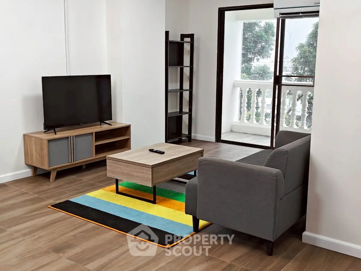 Modern living room with balcony, featuring sleek furniture and vibrant rug.
