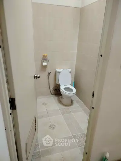 Compact bathroom with tiled walls and floor, featuring a toilet and basic amenities.