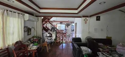 Spacious living room with wooden flooring and staircase, featuring cozy seating and natural light.