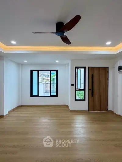 Spacious modern living room with wooden flooring and ceiling fan, featuring large windows for natural light.