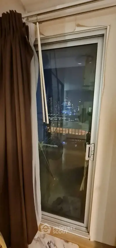 Cozy apartment with balcony offering stunning city night view through glass door.