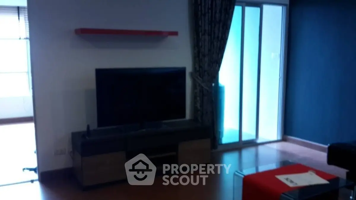 Modern living room with TV and sliding glass doors leading to balcony.