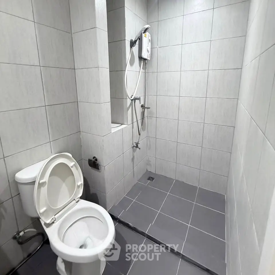 Modern bathroom with tiled walls and electric shower in a real estate property.