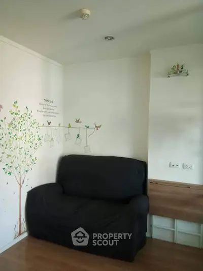 Cozy living room corner with black sofa and decorative wall art in modern apartment.