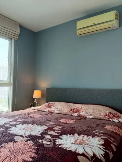 Cozy bedroom with floral bedding and air conditioning, offering a serene city view.