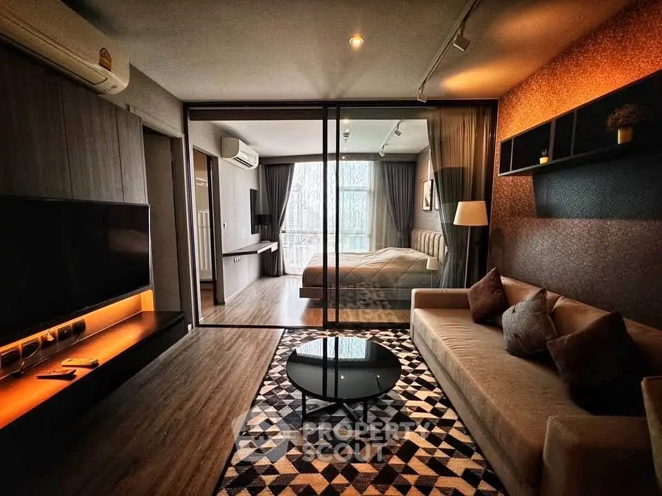 Modern living room with stylish decor and glass partition leading to a cozy bedroom.