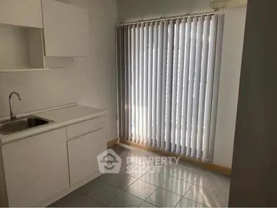 Bright kitchen area with vertical blinds and white cabinetry