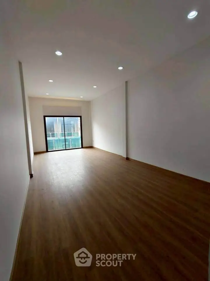 Spacious empty room with wooden flooring and large window, ideal for customization.