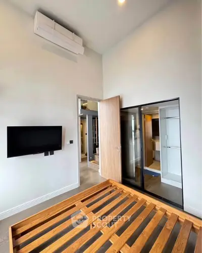 Modern bedroom with wooden bed frame, wall-mounted TV, and glass door to ensuite bathroom.