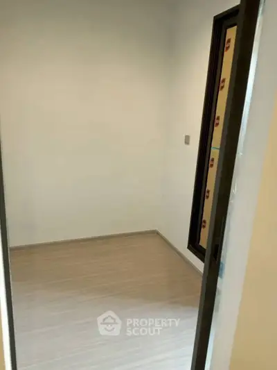 Minimalist small room with wooden flooring and a single window, perfect for storage or study.
