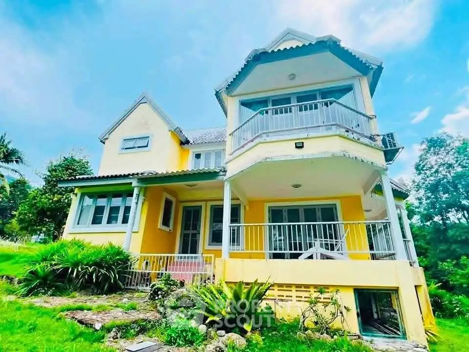 Charming yellow two-story house with lush garden and spacious balcony, perfect for serene living.