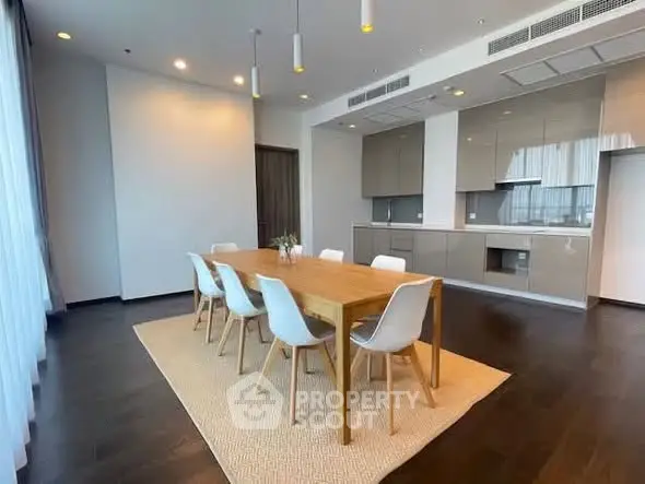 Spacious modern dining area with sleek kitchen in open layout, featuring elegant wooden table and chairs.