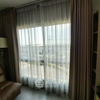 Cozy living room with large window and sheer curtains offering a city view