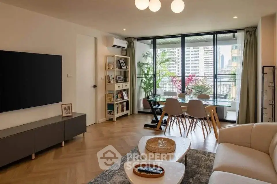 Modern living room with large TV, stylish furniture, and city view balcony.