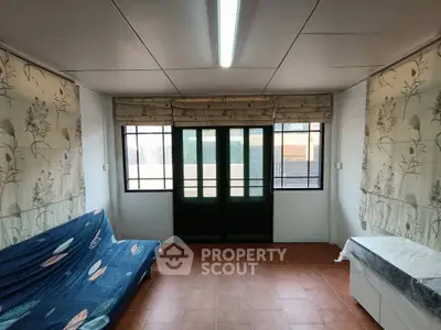 Cozy living room with large windows and floral curtains, featuring a comfortable sofa and tiled flooring.