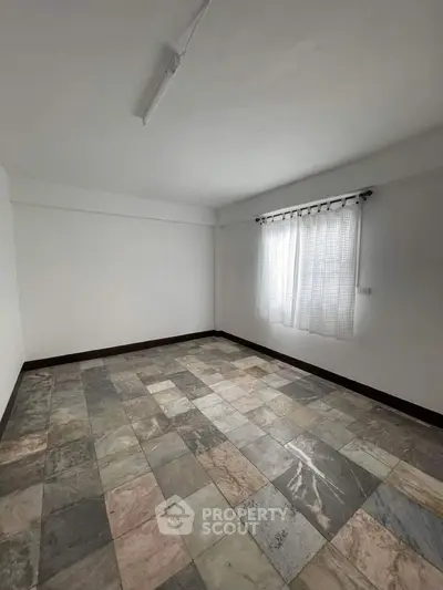 Spacious empty room with tiled flooring and natural light through window.