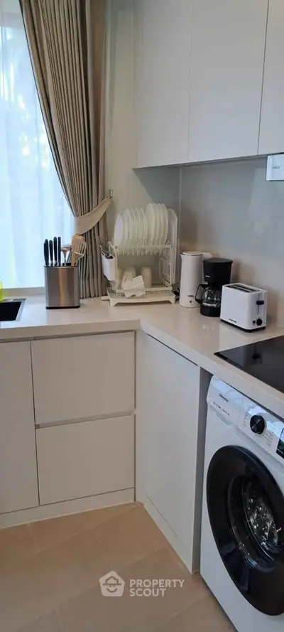 Modern kitchen with washing machine, sleek cabinets, and natural light