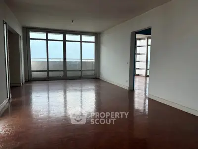 Spacious empty living room with large windows and wooden flooring, offering potential for customization.