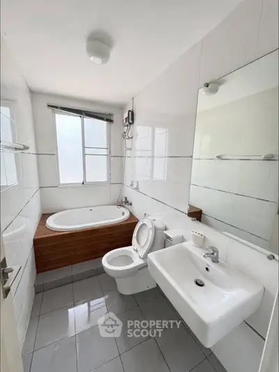 Modern bathroom with bathtub, toilet, and sink in a bright, tiled space.