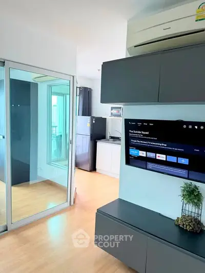 Modern living room with sleek cabinetry and wall-mounted TV, adjacent to a compact kitchen area.