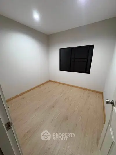 Spacious empty room with wooden flooring and a large window, perfect for customization.