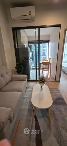 Modern living room with cozy sofa and glass partition leading to a bright balcony view.