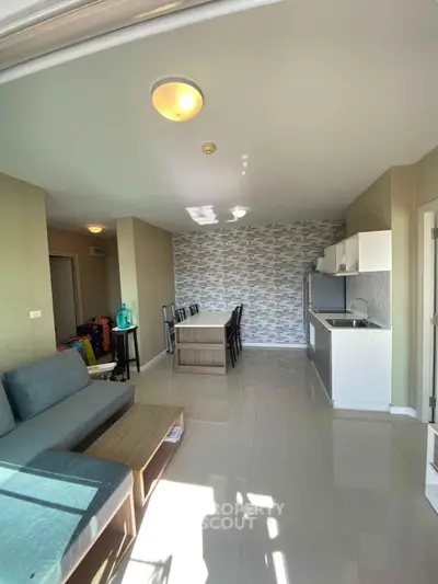 Modern open-plan living room with stylish kitchen and dining area, featuring sleek furniture and ample natural light.