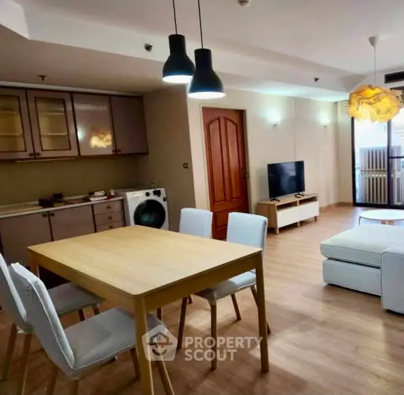 Spacious modern living room with dining area and washer, featuring stylish lighting and wooden flooring.