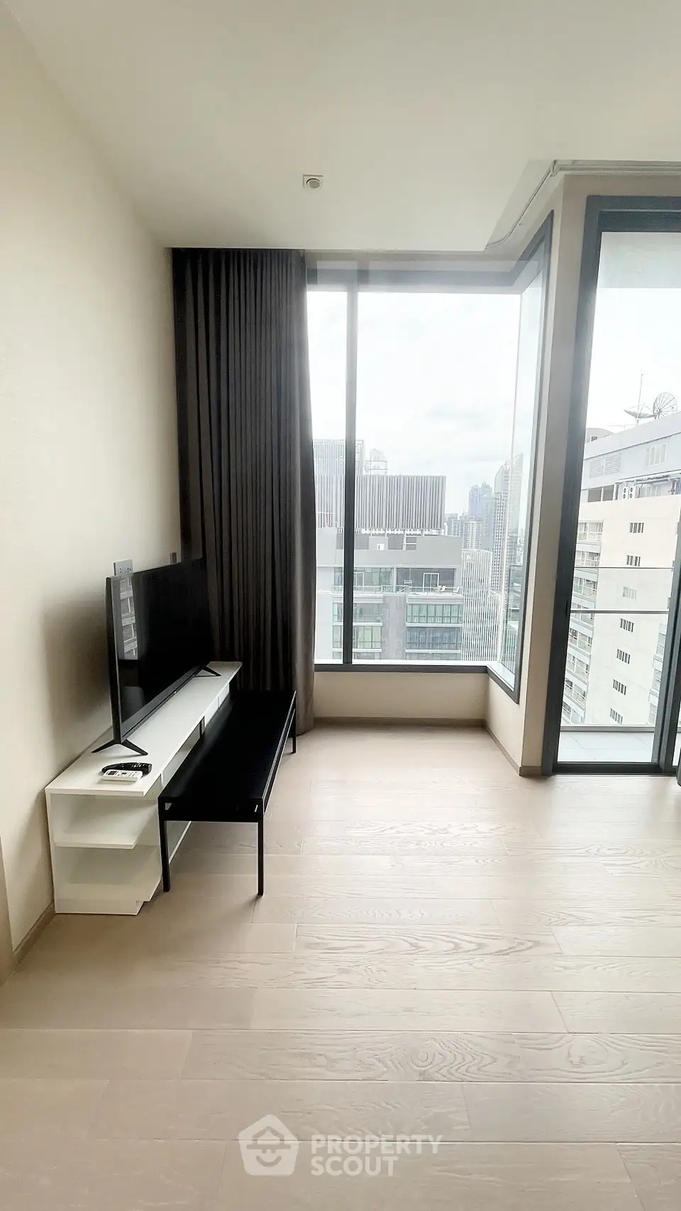 Modern living room with large windows offering city views, featuring sleek TV stand and minimalist decor.