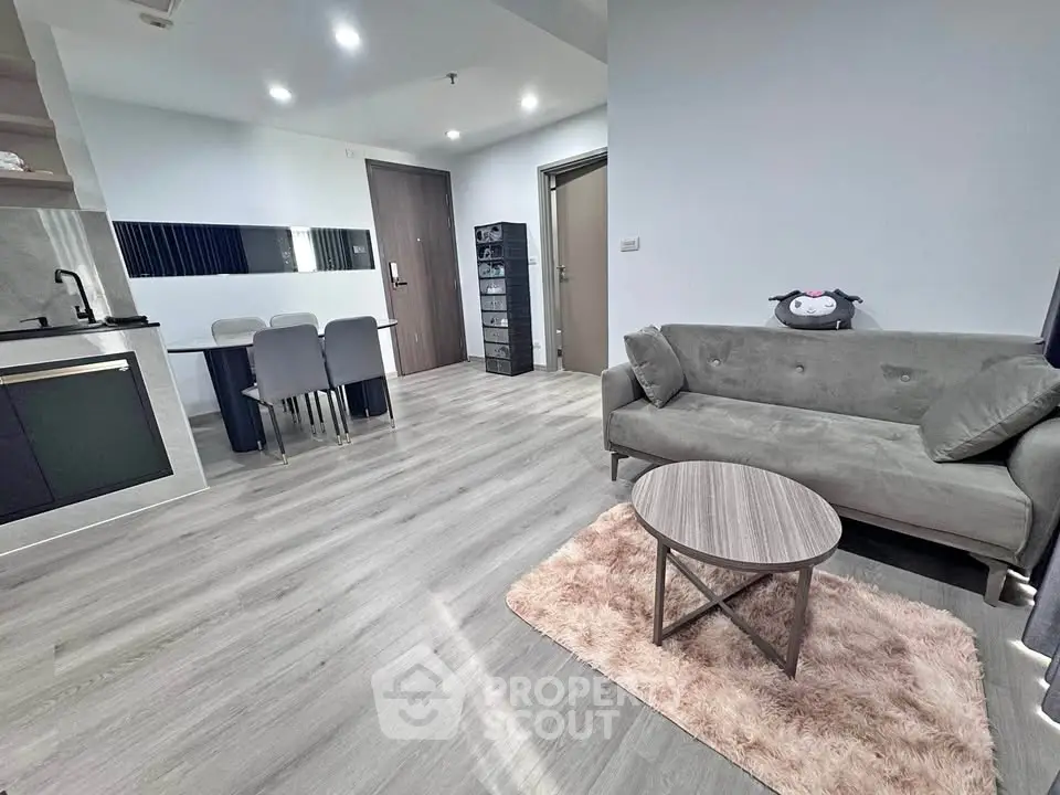 Modern open-plan living room with sleek kitchen and dining area, featuring stylish furniture and elegant flooring.