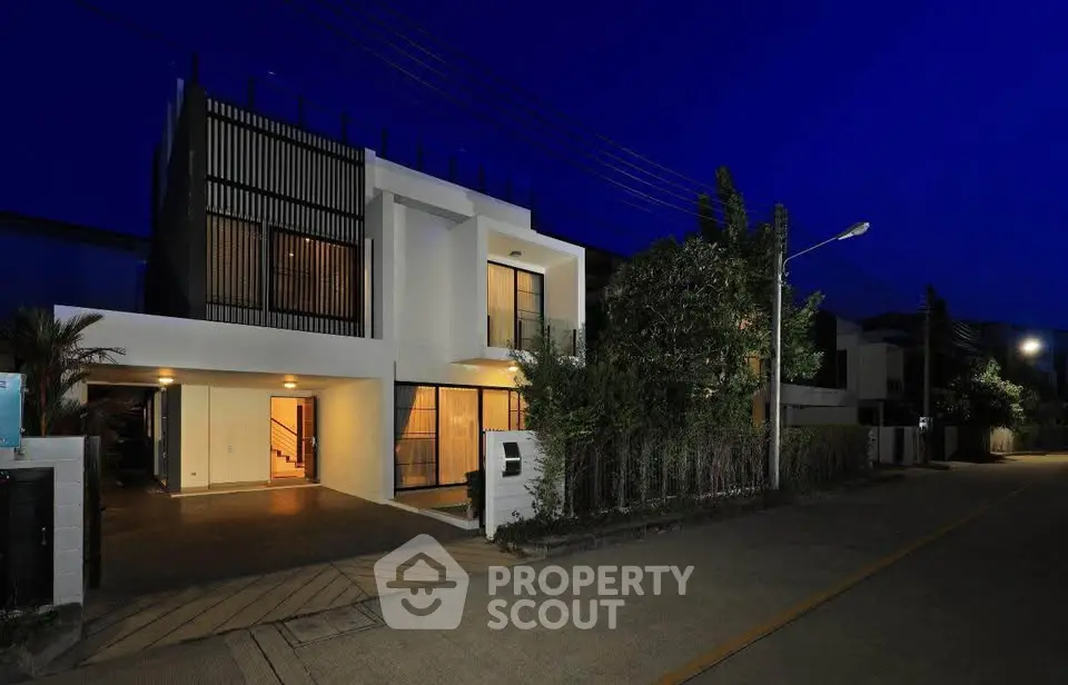 Modern two-story house with sleek design and illuminated entrance at night.