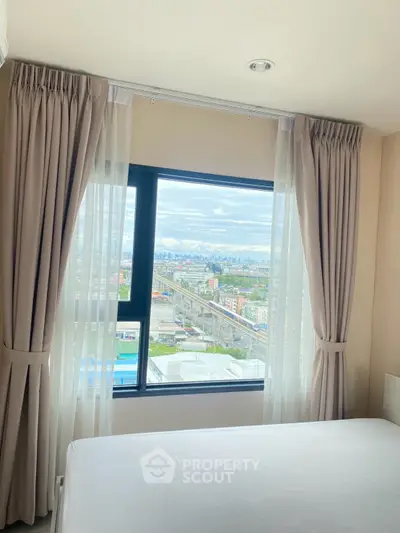 Bright bedroom with large window offering stunning city view, perfect for urban living.