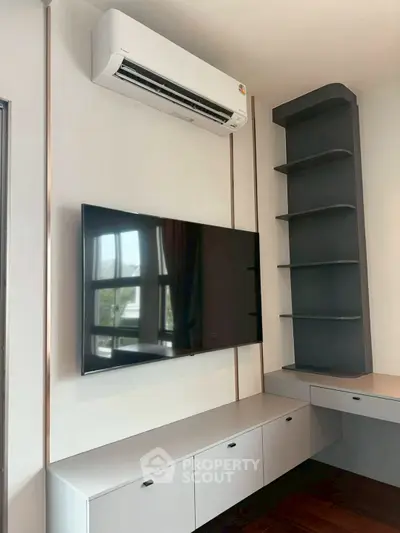 Modern living room with wall-mounted TV and air conditioning unit, featuring sleek storage cabinets and shelves.
