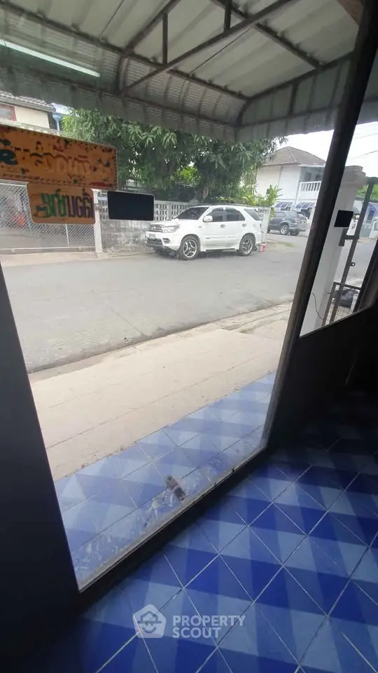Street view from a building entrance with blue tiled floor and parked car outside.