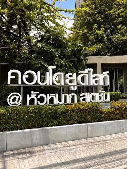 Modern condominium entrance with lush greenery and sleek signage in urban setting.