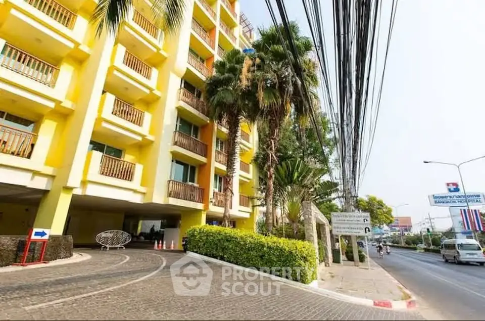 Vibrant yellow apartment building with lush palm trees and street view