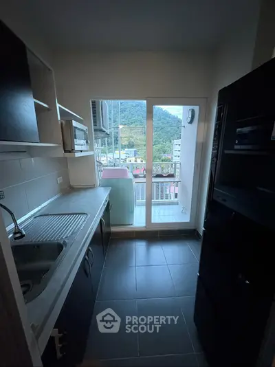 Modern kitchen with sleek appliances and balcony view of lush green hills.