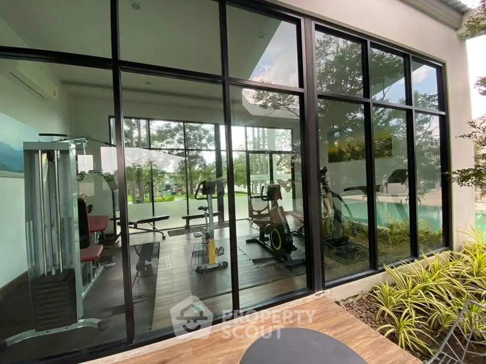 Modern gym with large windows overlooking lush greenery and pool, perfect for fitness enthusiasts.
