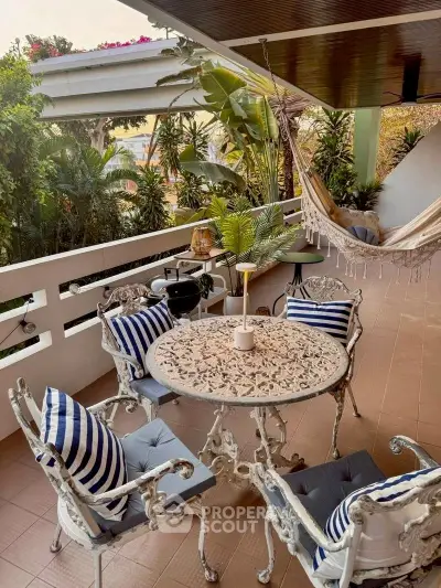 Charming balcony with elegant furniture and hammock, surrounded by lush greenery.