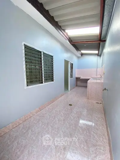 Spacious tiled utility area with sink and natural light, perfect for laundry or storage.