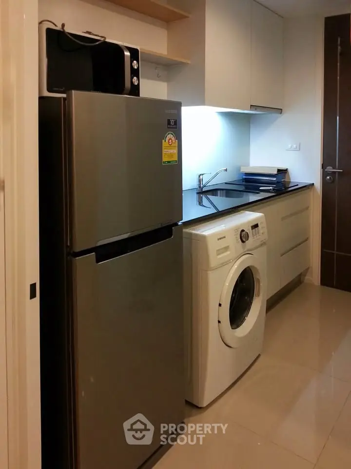 Modern kitchen with sleek appliances including fridge, washing machine, and microwave in compact layout.