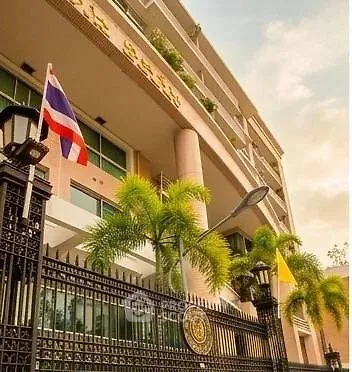 Elegant building exterior with lush palm trees and national flags, showcasing modern architecture and secure entrance.