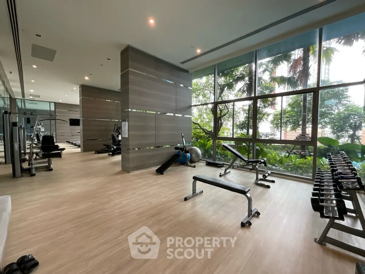 Spacious modern gym with large windows and lush greenery view, perfect for fitness enthusiasts.