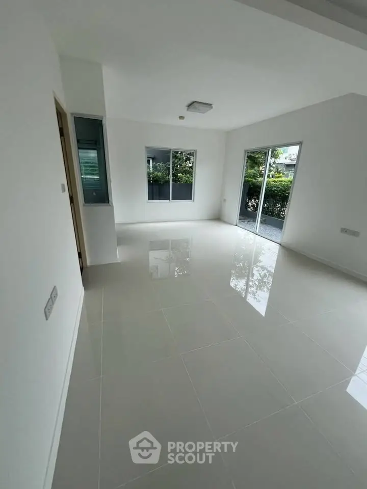 Spacious modern living room with large windows and glossy tiled floors, offering abundant natural light.