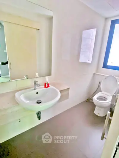 Modern bathroom with sleek sink and toilet, featuring a large mirror and natural light from window.