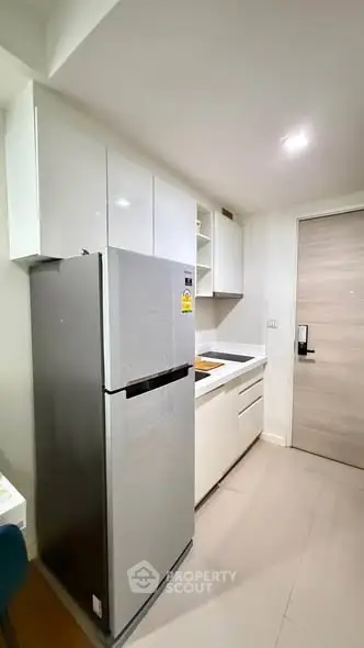 Modern compact kitchen with sleek cabinetry and stainless steel fridge in a stylish apartment.
